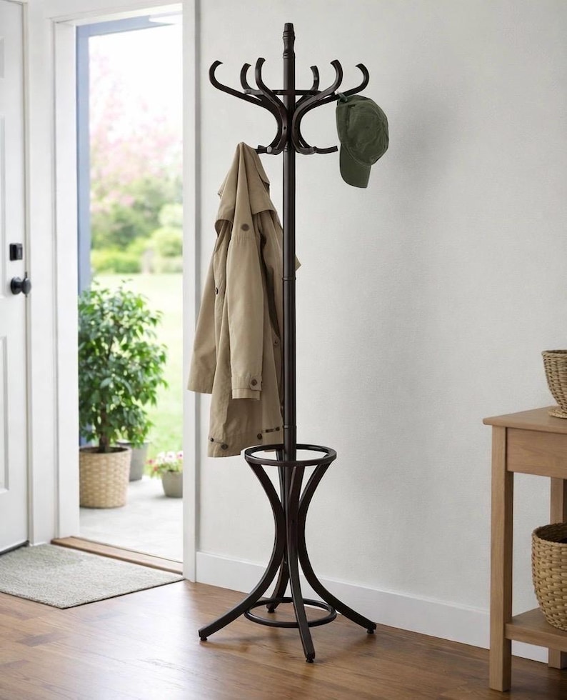 May include: A dark brown metal coat rack with multiple curved hooks at the top. A tan coat and a green baseball cap hang from the hooks. The rack has a circular base and a decorative support.