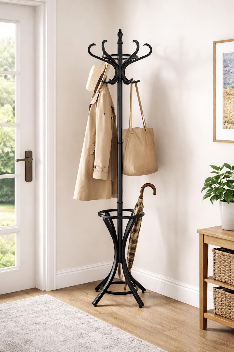 May include: A black metal coat rack with multiple hooks for hanging coats, hats, and bags. A tan trench coat, a beige tote bag, and a straw hat hang from the hooks. An umbrella rests in the base of the rack. The rack is in a home entryway.