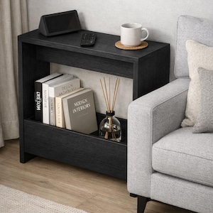 May include: A black side table with a shelf, holding books, a diffuser, and a decorative cup. A remote and a small speaker sit on top. The table is next to a gray sofa and a rug.