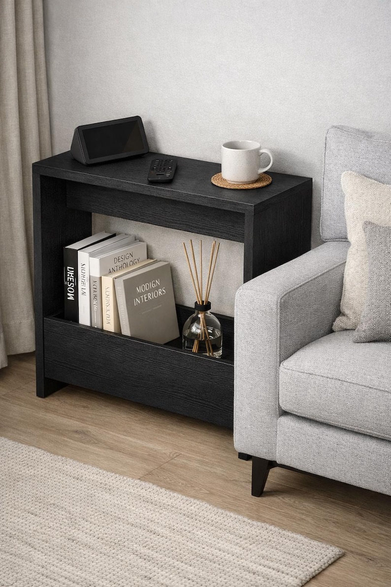 May include: A black side table with a shelf, holding books, a diffuser, and a decorative cup. A remote and a small speaker sit on top. The table is next to a gray sofa and a rug.