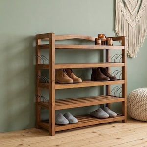 May include: A wooden shoe rack with four shelves, holding various pairs of shoes and slippers. The rack is made of light brown wood and has a simple, functional design. The background features a green wall and a decorative wall hanging.
