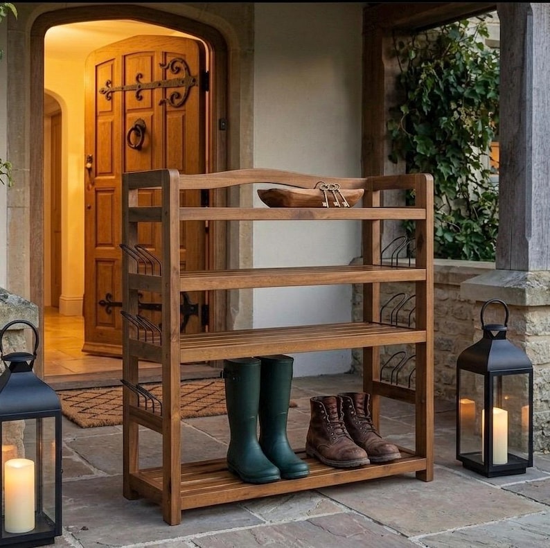 May include: A wooden shoe rack with four shelves, holding green rain boots and brown leather boots. The top shelf has a wooden bowl and keys. The rack is outside a doorway, with lanterns on either side.