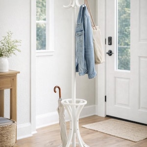 May include: A white coat rack with multiple curved hooks, a central pole, and a circular base. A denim jacket, a beige tote bag, and a light-colored umbrella hang from the rack. The rack is in a bright entryway with a wooden floor.