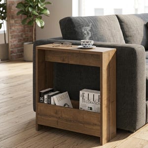 May include: A wooden side table with a magazine rack. The table is a warm brown colour and has a rectangular shape. A cup of coffee and eyeglasses sit on top. Magazines and books are visible in the rack.