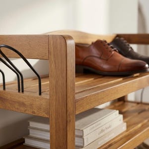 May include: A wooden shoe rack with two pairs of leather shoes. The rack is made of light brown wood and has multiple shelves. The shoes are brown and black. There are also some books on the bottom shelf.