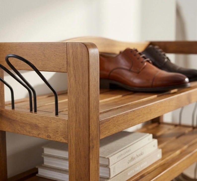 May include: A wooden shoe rack with two pairs of leather shoes. The rack is made of light brown wood and has multiple shelves. The shoes are brown and black. There are also some books on the bottom shelf.