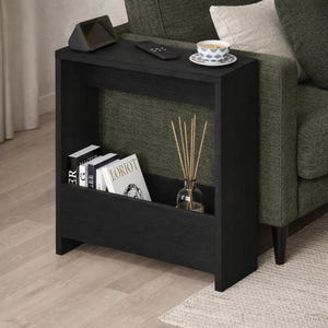 May include: A black side table with a built-in shelf, holding books and a glass diffuser with reeds. A small speaker, remote, and teacup sit on top. The table is positioned next to a green sofa.