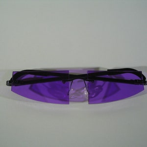 May include: A pair of rimless sunglasses with purple lenses and a black frame. The lenses are rectangular with a curved bottom edge. The temples are black and connect to the lenses with small hinges.