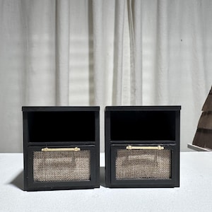 May include: Two miniature black nightstands with open top shelves and lower drawers with woven fabric fronts and brass handles. The nightstands are set against a white backdrop.