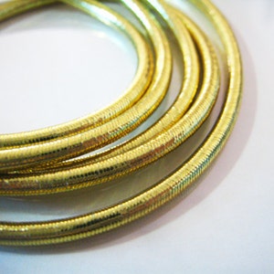 May include: Close-up of a gold-colored, braided cord with a shiny, textured surface.