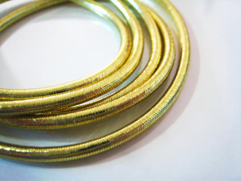 May include: Close-up of a gold-colored, braided cord with a shiny, textured surface.