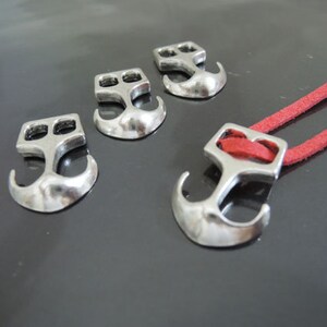 May include: Four silver anchor-shaped clasps with a red cord threaded through one of the clasps.