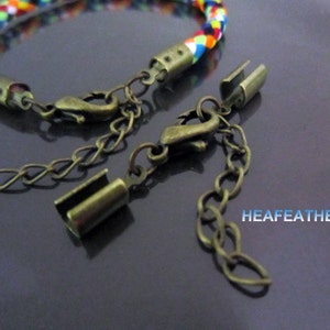 May include: A colorful braided bracelet with a bronze clasp and extender chain. The bracelet is made of multiple strands of colorful thread woven together.