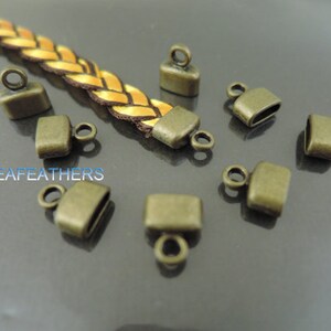 May include: A close-up of ten antique gold-toned metal end caps with a loop for attaching to a cord or strap. The end caps are square with rounded corners and have a smooth finish.