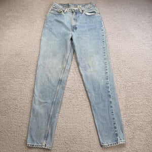 May include: Light blue denim jeans with a classic five-pocket design. The jeans have a straight leg cut and a button and zipper closure. The denim has a faded wash, giving them a worn-in look. The jeans are laid flat on a neutral surface.