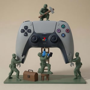Puede incluir: Un soporte para mando de videojuegos gris y negro con cuatro soldados de juguete de pl&aacute;stico verde. Un soldado est&aacute; sentado encima con un martillo, dos sostienen llaves inglesas a los lados y uno en una escalera usa un taladro azul.