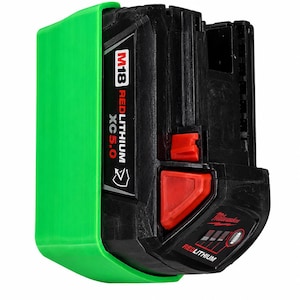 Pode incluir: Uma bateria preta Milwaukee M18 REDLITHIUM XC 5.0 com uma capa de plástico verde brilhante fixada na lateral. A bateria possui botões de liberação vermelhos, um indicador de carga e texto em branco e vermelho na carcaça.