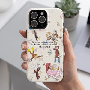 May include: A cream-colored phone case featuring a pattern of Curious George illustrations, including the monkey scuba diving, eating, and playing. The text reads: Be joyful in hope, patient in affliction, faithful in prayer. Romans 12:12.