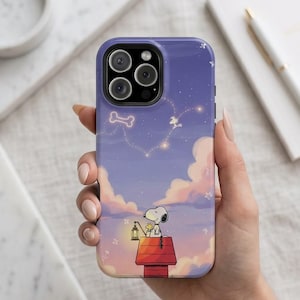 May include: A purple smartphone case featuring a graphic of Snoopy and Woodstock sitting on a red doghouse at sunset. The sky is filled with soft pink and orange clouds, with a constellation shaped like a bone and a small glowing lantern.