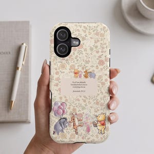 May include: A cream-colored phone case featuring a delicate floral pattern in soft pink, orange, and green. It displays illustrations of Winnie the Pooh characters and the text: God has already handled what you're worrying about. Jeremiah 29:11.