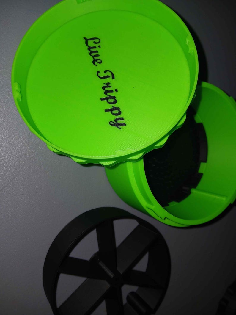 May include: Bright green container with a lid, featuring the text "Live Trippy" in black script. The container is open, revealing a dark interior. A black, circular object with spokes is also visible.