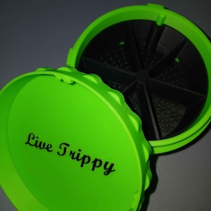 May include: Bright green container with a lid that reads "Live Trippy" in black script. The container is open, revealing a black interior divided into sections. The lid has a textured edge.