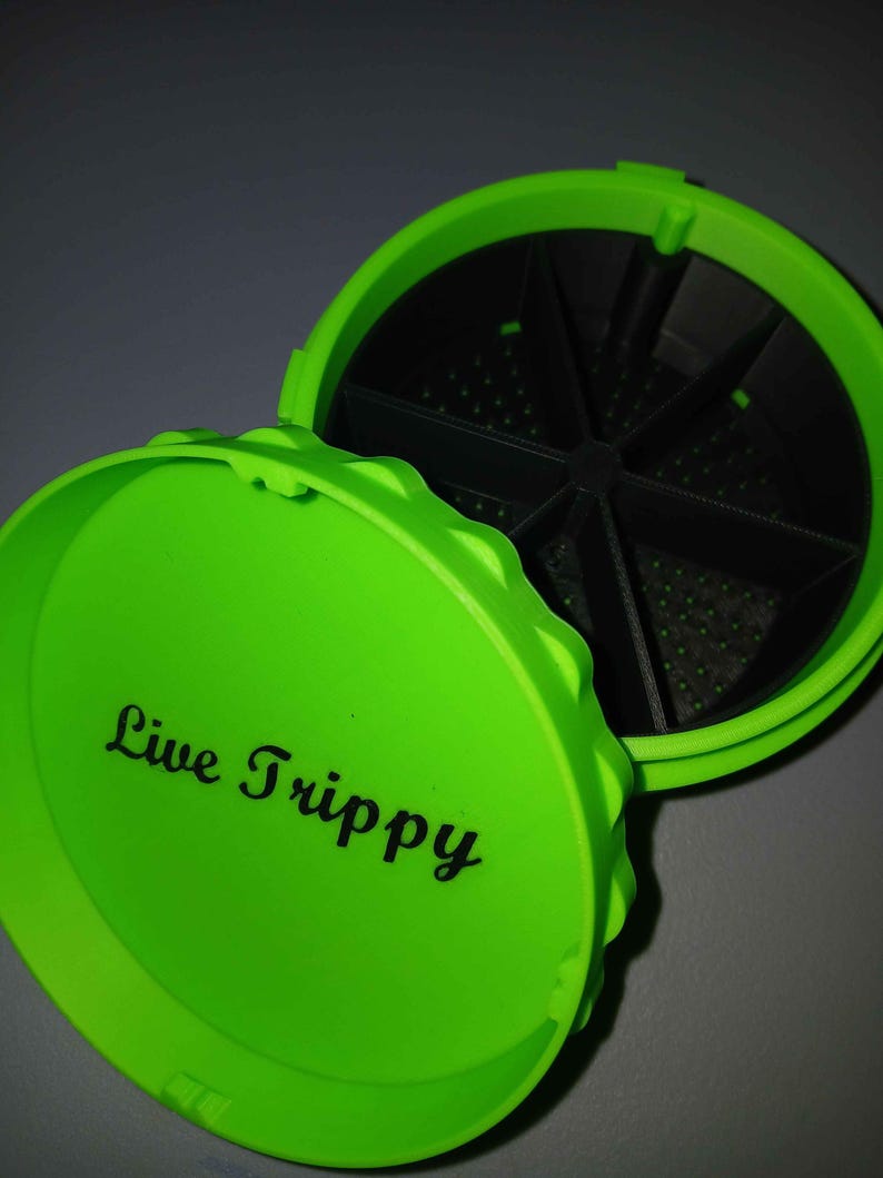 May include: Bright green container with a lid that reads "Live Trippy" in black script. The container is open, revealing a black interior divided into sections. The lid has a textured edge.