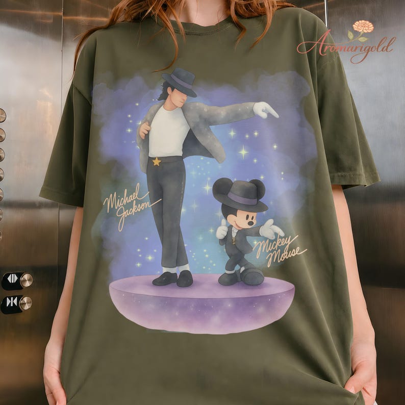 May include: Olive green t-shirt featuring a graphic of Michael Jackson and Mickey Mouse in a stylized design. The text "Michael Jackson" and "Mickey Mouse" are also visible. The shirt has short sleeves and a relaxed fit.