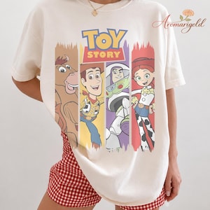 Puede incluir: Camiseta color crema con el logo y los personajes de Toy Story. El dise&ntilde;o incluye a Woody, Buzz Lightyear, Jessie y Bullseye, cada uno en un bloque de color vertical. La camiseta es de corte holgado.
