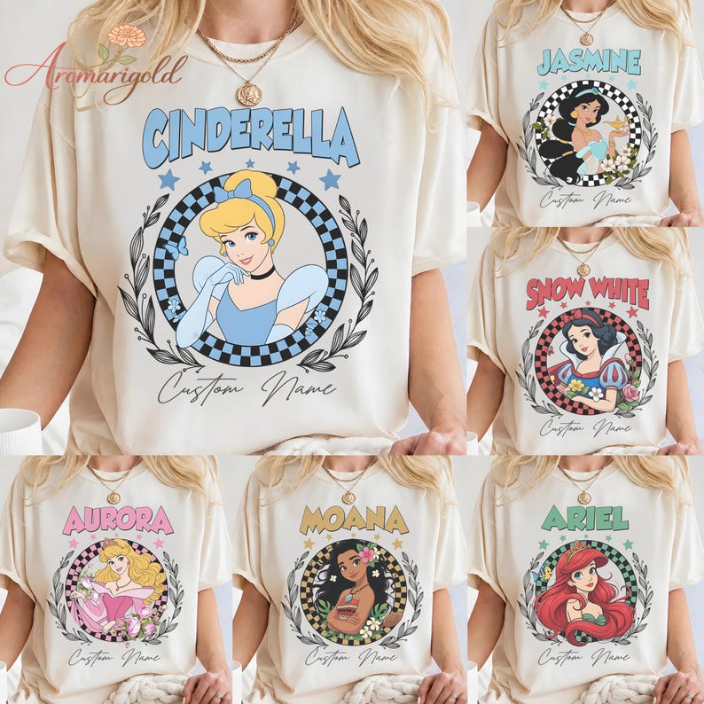 May include: Cream-coloured t-shirts featuring Disney princesses: Cinderella, Jasmine, Snow White, Aurora, Moana, and Ariel. Each shirt has a princess graphic within a circular design, with the princess's name above and "Custom Name" below.