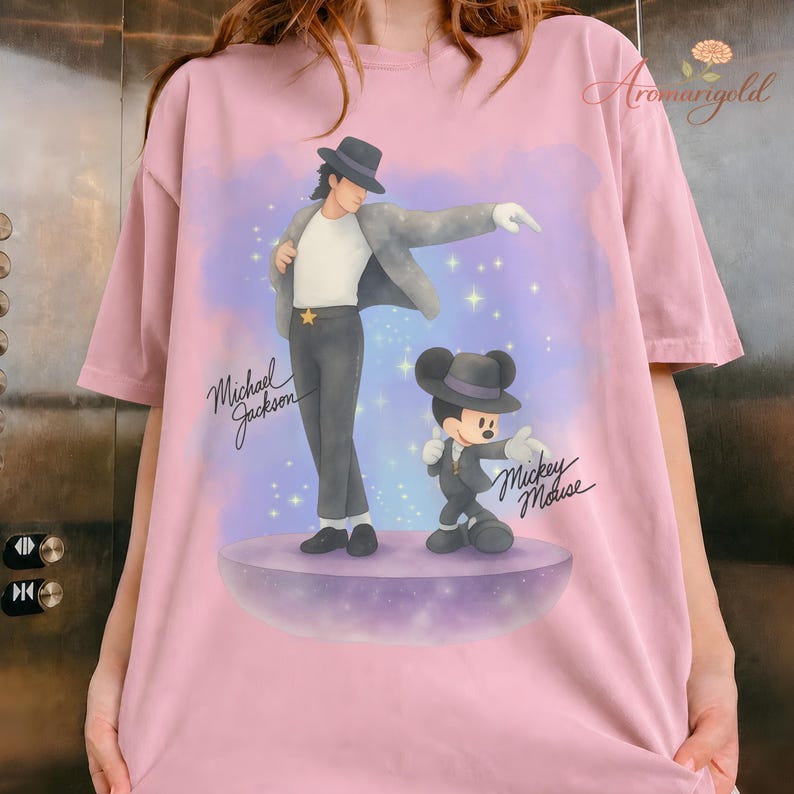 May include: Pink t-shirt featuring a graphic of Michael Jackson and Mickey Mouse in matching outfits. The design includes the text "Michael Jackson" and "Mickey Mouse" in cursive, set against a purple and blue background with stars.