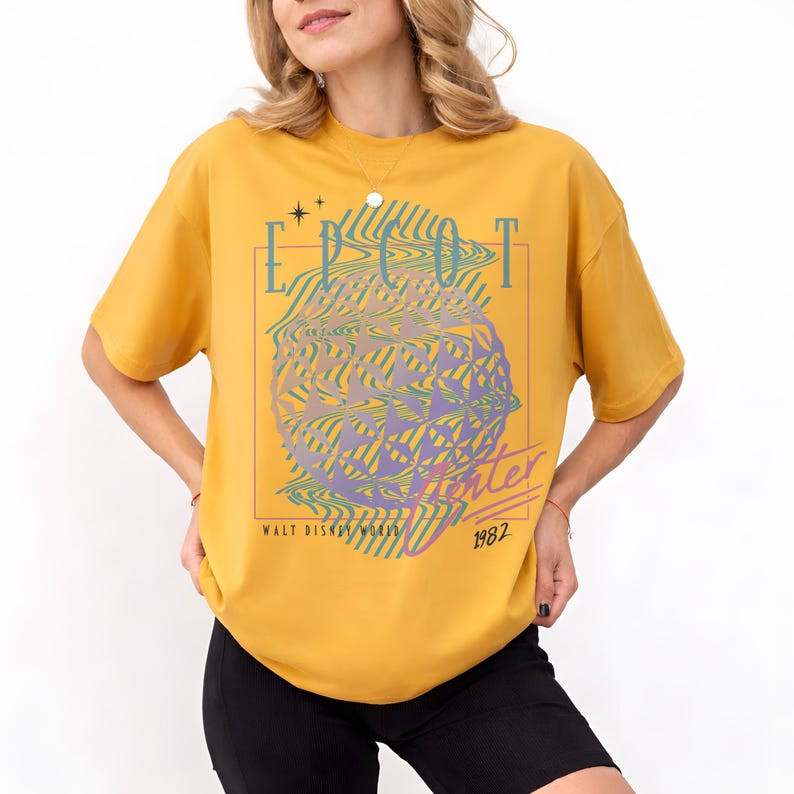 May include: Mustard yellow t-shirt featuring a graphic design with the text "EPCOT Center" in a retro style. The design includes a stylized globe and the text "Walt Disney World 1982".