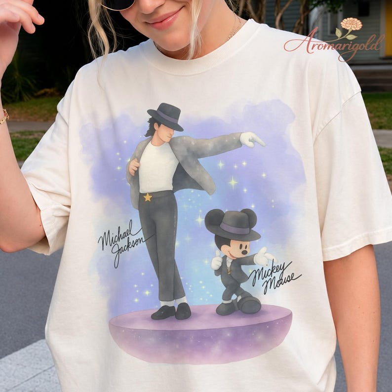 May include: Cream-colored t-shirt featuring a graphic of Michael Jackson and Mickey Mouse in matching outfits. The design includes the text "Michael Jackson" and "Mickey Mouse" in script. The background has a purple and blue watercolor effect with stars.