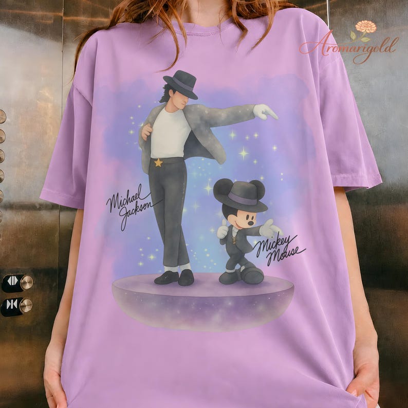 May include: A light purple t-shirt featuring a graphic of Michael Jackson and Mickey Mouse in matching outfits. The text "Michael Jackson" and "Mickey Mouse" are written in cursive. The background is a purple and blue gradient with stars.