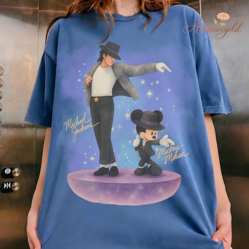 May include: Blue t-shirt featuring a graphic of Michael Jackson and Mickey Mouse in a performance pose. The text "Michael Jackson" and "Mickey Mouse" are written in gold script. The design is set against a starry, purple background.