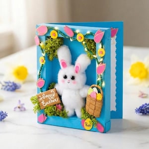 May include: A blue Easter card featuring a fluffy white bunny holding a basket of eggs and a sign that says "Happy Easter." The card is decorated with pink tulips, yellow flowers, and green moss. A string of lights is wrapped around the frame.