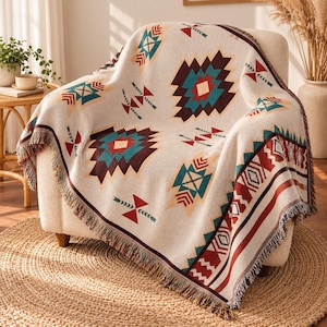 Può includere: Una coperta tessuta color crema caratterizzata da un motivo geometrico ripetuto nelle tonalità del marrone scuro, ottanio e rosso. La coperta presenta un bordo sfrangiato ed è drappeggiata su una poltrona chiara, mettendo in risalto il design.