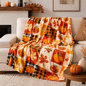 Pode incluir: Uma manta macia com um padrão de patchwork de abóboras cor de laranja, lanternas de Halloween, folhas de ácer de outono e quadrados axadrezados a preto e branco. O tecido apresenta um design sazonal repetitivo em tons de laranja, creme e preto.
