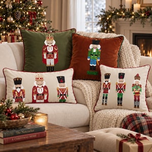 May include: Four decorative throw pillows featuring embroidered nutcracker figures. One olive green square pillow, one rust orange square pillow, one cream rectangular pillow with three nutcrackers, and one cream square pillow with three nutcrackers.