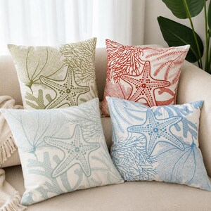 May include: A set of four square scatter cushions featuring embroidered marine designs on a white background. Each cushion displays a unique starfish and coral pattern in distinct colours: olive green, bright red, light blue, and dark blue.