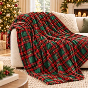 Könnte beinhalten: Eine weiche Wohndecke mit einem klassischen Schottenkaro-Muster in leuchtendem Rot, Tannengrün und Schwarz. Der weiche, strukturierte Stoff liegt über einem hellen Sofa und zeigt die sich kreuzenden Linien und die tiefe Farbpalette.
