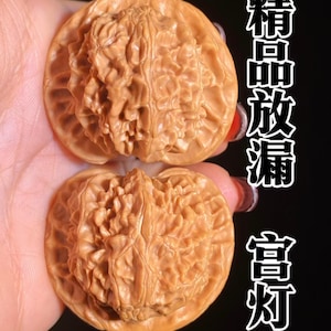 May include: Two light brown, textured walnut shells with intricate, deep ridges and a natural, woody appearance. The shells are displayed together, featuring a complex, brain-like surface pattern. The Chinese characters 精品放漏 富灯 are visible in white text on the right side.
