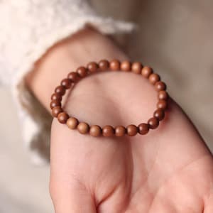 May include: A brown wooden bead bracelet. The bracelet is made of small, round, polished wooden beads strung together. The beads are a warm, medium brown color. The bracelet is worn on a wrist.