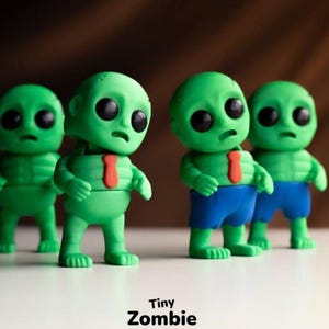May include: Four small green zombie figurines with large black eyes and sad expressions. Two figures wear blue shorts, one has a red tie, and one is plain. The text Tiny Zombie is printed at the bottom center of the image in black lettering.