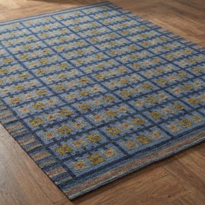 Op de afbeelding: Een rechthoekig vloerkleed met een ruitpatroon in blauwtinten. Het ontwerp bestaat uit donkerblauwe kruisende lijnen die vierkanten vormen, elk met kleine gele en oranje geometrische motieven over het gehele oppervlak.