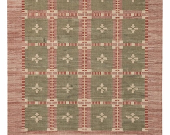 Op de afbeelding: Een rechthoekig vloerkleed met een rasterpatroon van olijfgroene vierkanten gescheiden door verticale en horizontale banden in rood en crème. Elk groen vierkant bevat een klein crèmekleurig kruis. Het kleed heeft franjes.