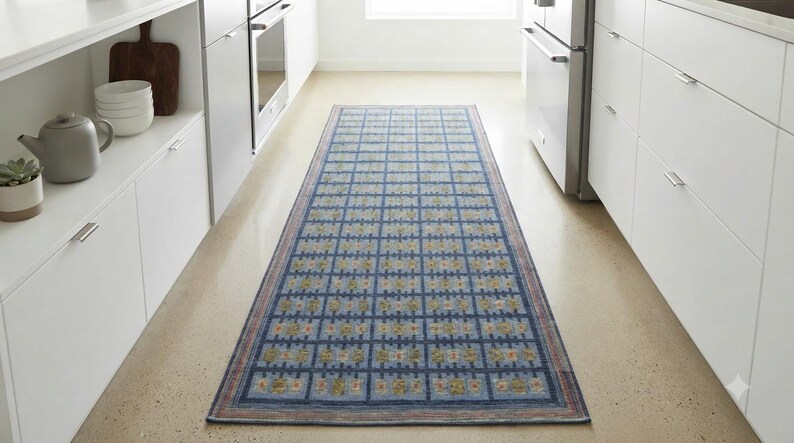 Op de afbeelding: Een rechthoekige loper met een blauwe achtergrond en een herhalend rasterpatroon van kleine, lichtgekleurde geometrische vormen en bloemachtige motieven, afgewerkt met een dunne, meerkleurige rand langs de zijkanten.