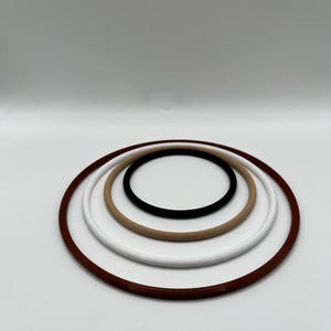 May include: A collection of rubber O-rings in various sizes and colors. The rings are arranged in a nested pattern, with a dark brown ring on the outside, followed by white, tan, and black rings. The background is plain white.