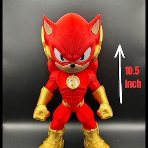 May include: A red and gold figurine of The Flash, standing approximately 26.7 cm tall. The figure has a red body with gold accents on the boots, gloves, and headgear. The Flash logo is on the chest.
