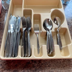 May include: A beige plastic cutlery tray organizer containing stainless steel flatware. The set includes knives, forks, and spoons, each featuring a subtle etched star pattern on the handle. The tray has multiple compartments for sorting.